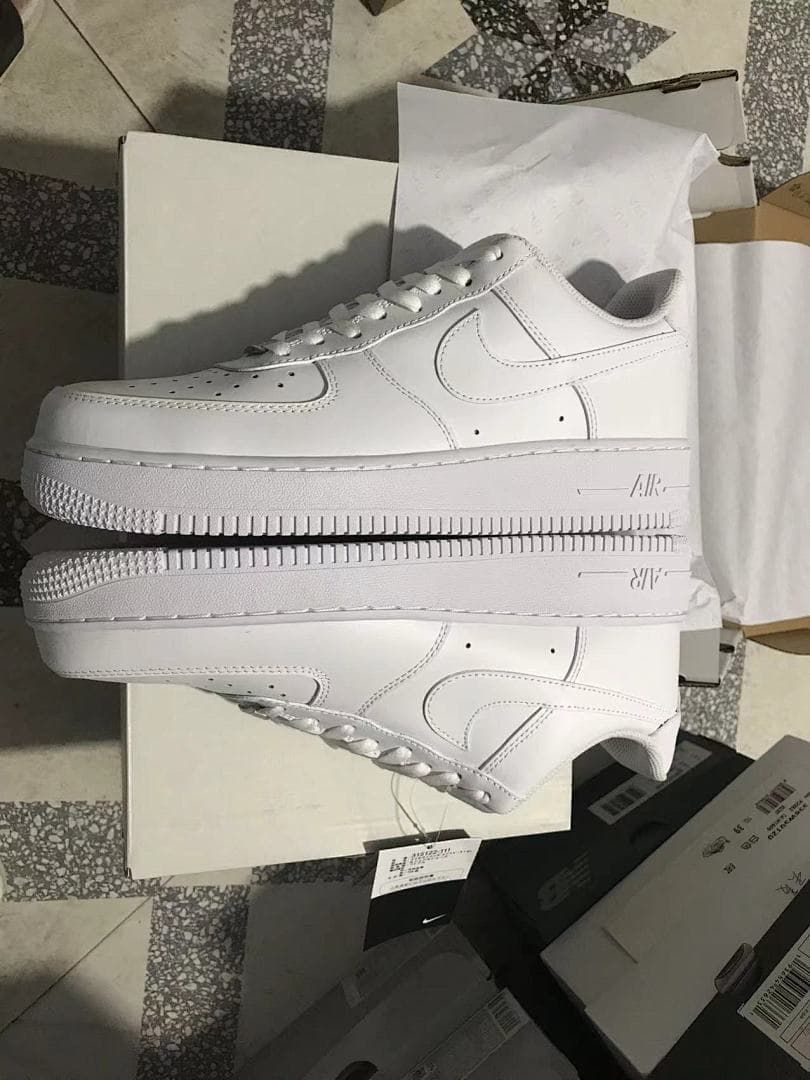 Pair of white sneakers arranged on a box, showing their side profiles and soles.