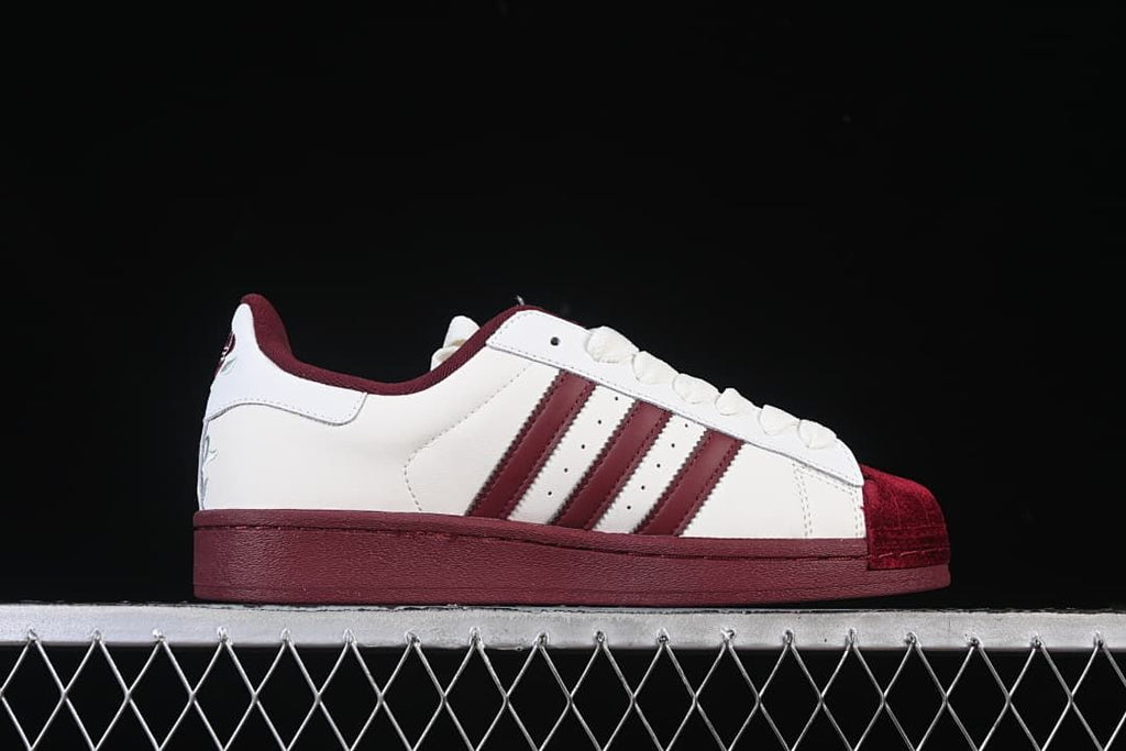 Side profile of the white low-top sneaker with burgundy stripes and sole.