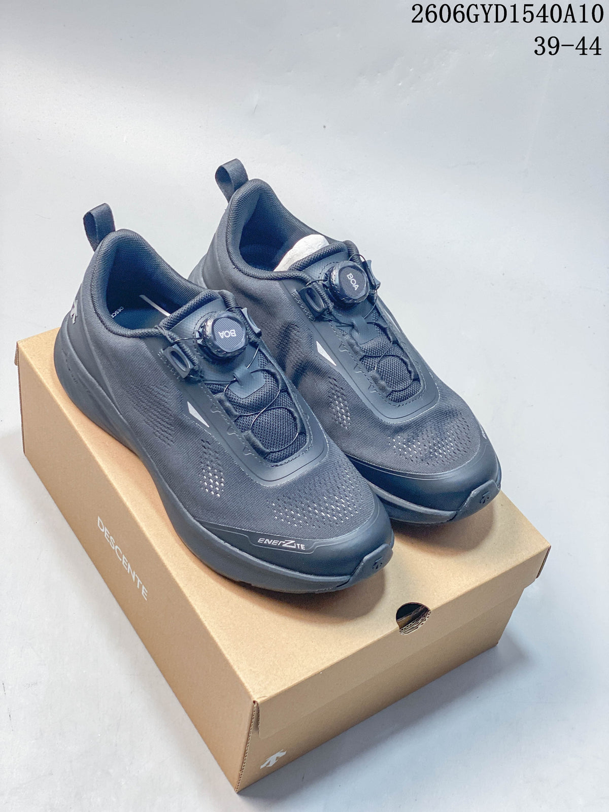 Pair of charcoal DESCENTE low-top running shoes with dial closures, shown on a branded box