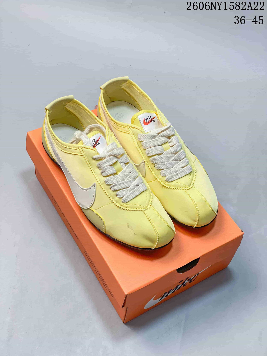 Yellow Nike low-top sneakers with light-colored Swooshes on an orange shoe box