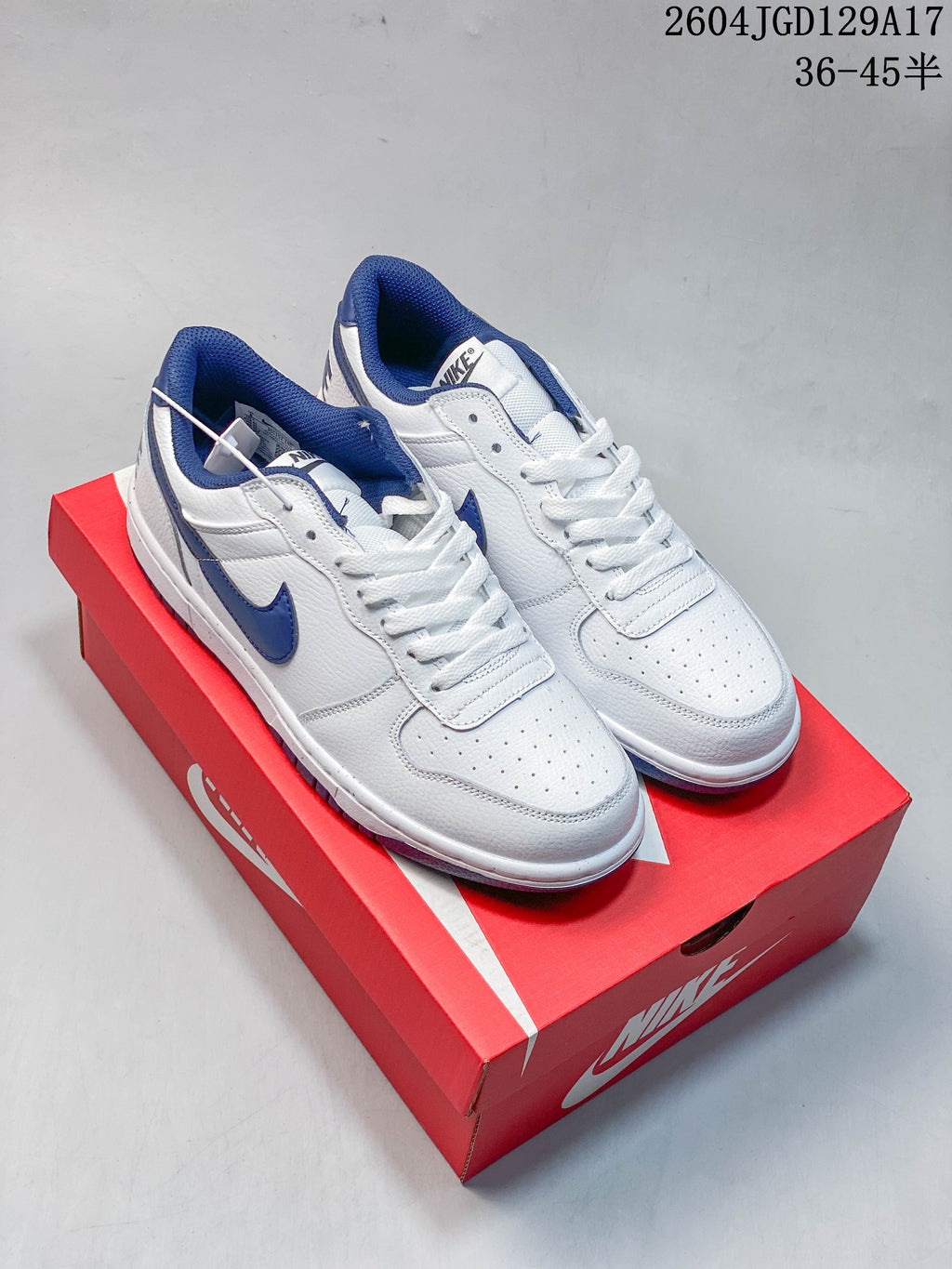 Pair of white and blue Nike Big Low low-top sneakers on a red shoebox