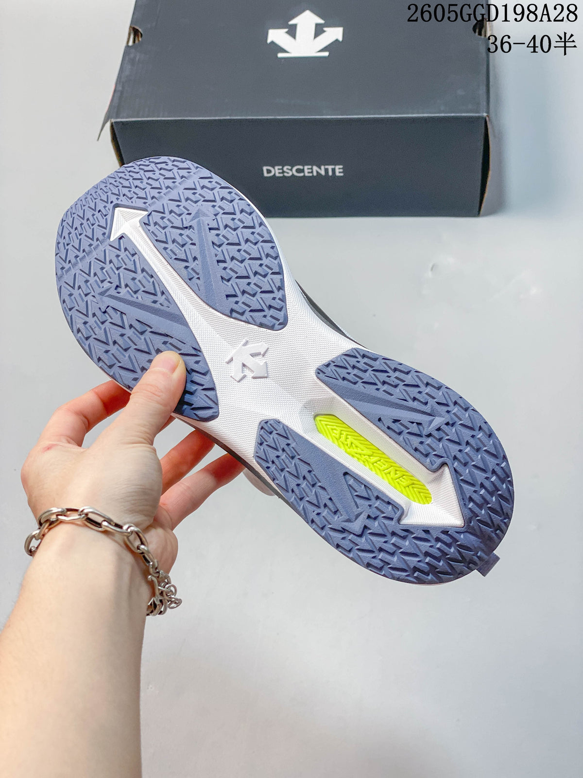Underside of the Descente running shoe showing a patterned blue-violet outsole and a bright accent in the midfoot; image overlay shows code 2605GGD198A28 and size range 36–40.5.