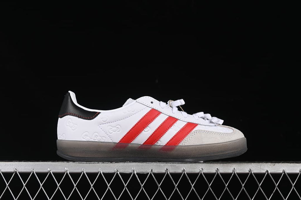 Side profile showing the white upper, red stripes, embossed Hello Kitty motifs, and grey-toned sole.