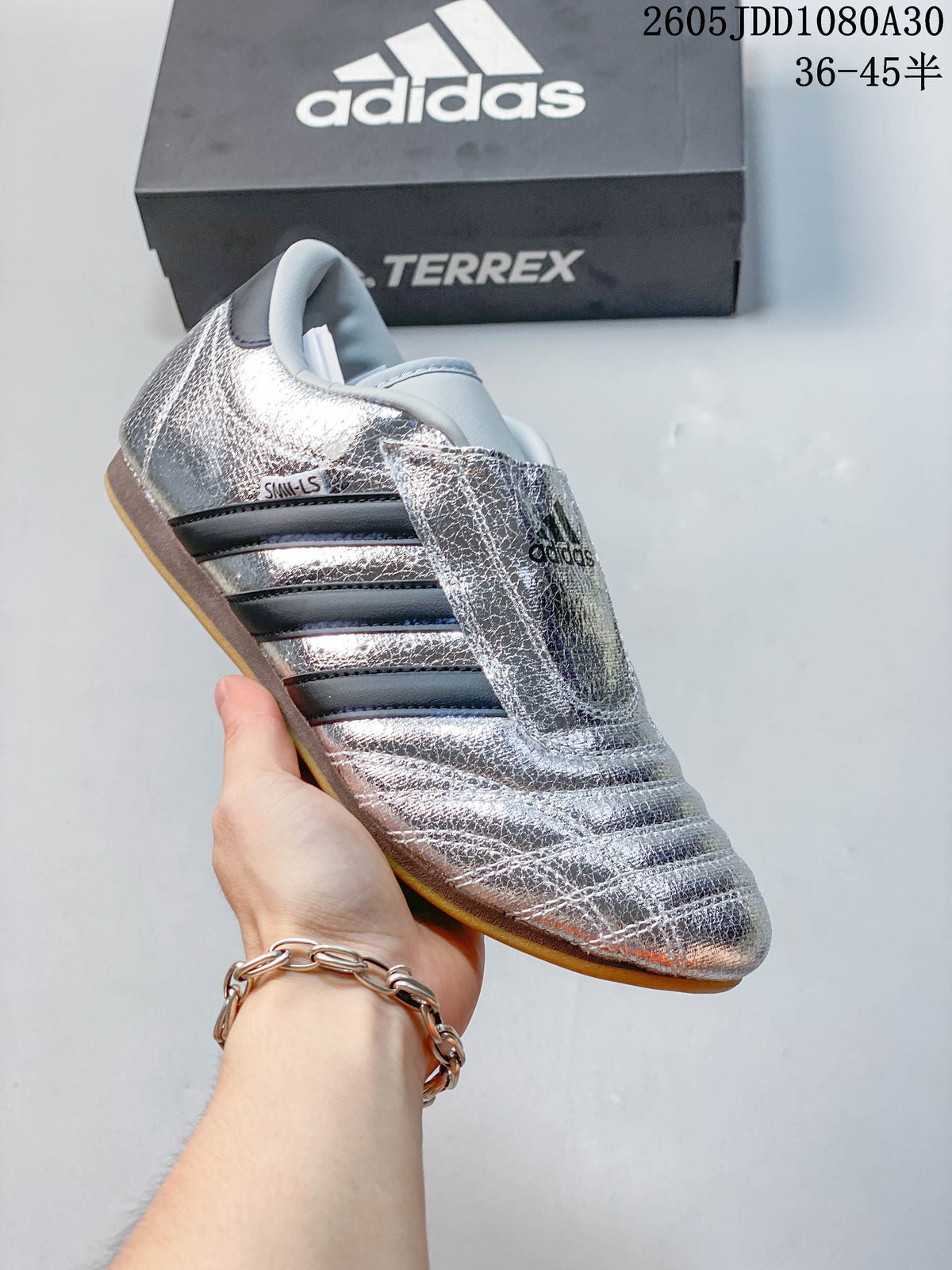 Angled side view of the silver shoe with dark stripes and gum-colored outsole