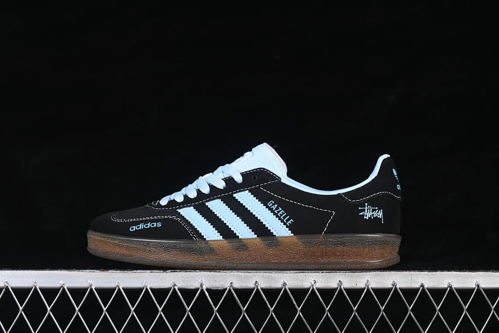Side view of a black adidas Gazelle Indoor sneaker with light blue stripes and a gum-colored sole