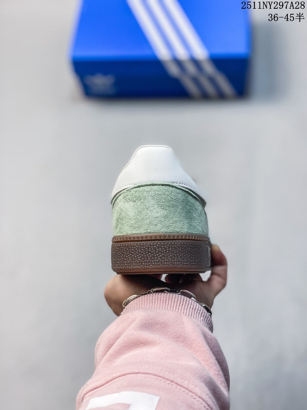 Rear view of a pale green adidas Handball Spezial sneaker with a white heel tab and brown outsole.