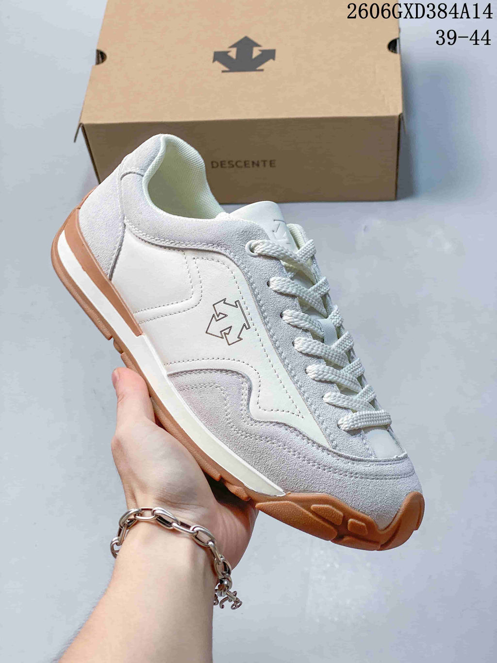 Angled side view of a white and light gray Descente sneaker with a gum-colored sole.
