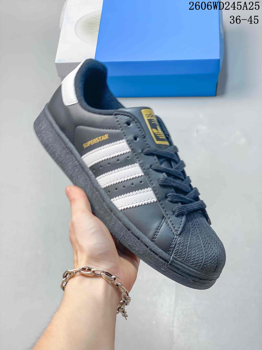 Side view of a charcoal Superstar sneaker with white stripes and a textured dark sole