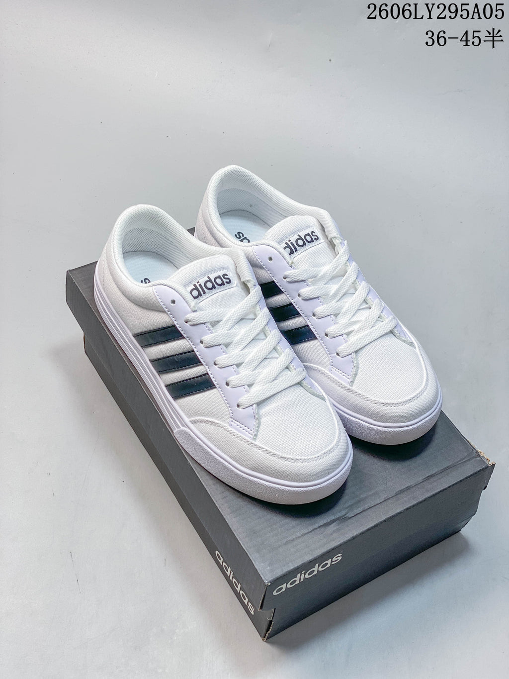 Pair of white adidas low-top sneakers with dark three-stripe side details.