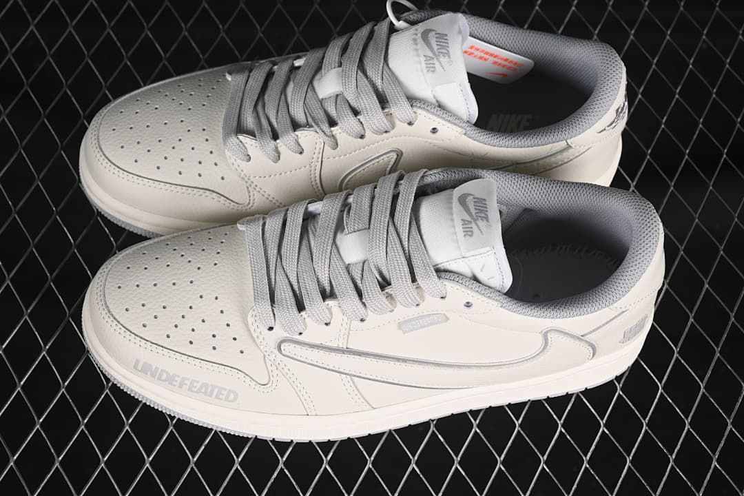 Pair of light neutral low-top sneakers shown from above, with gray laces, perforated toe panels, and padded collars.