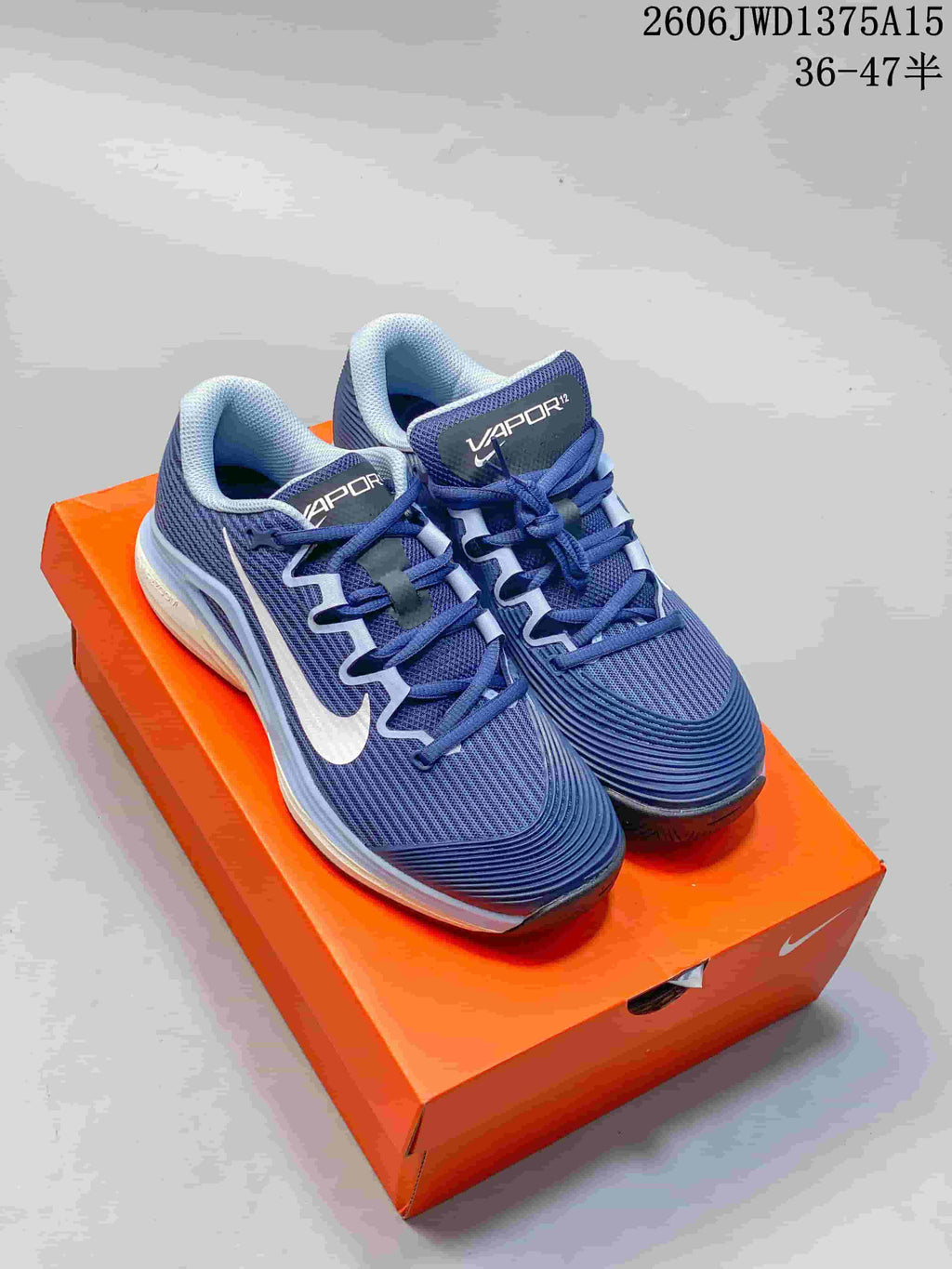 Pair of blue and white Nike Vapor 12 low-top tennis shoes on an orange shoebox