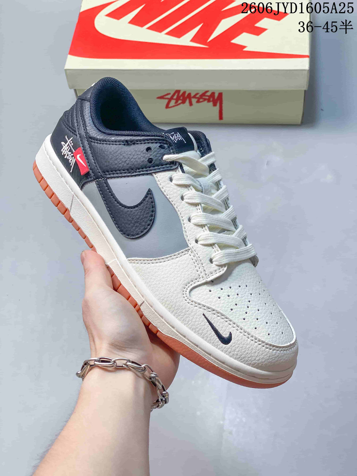 White and gray low-top sneaker with dark overlays, white laces, and a contrasting orange outsole