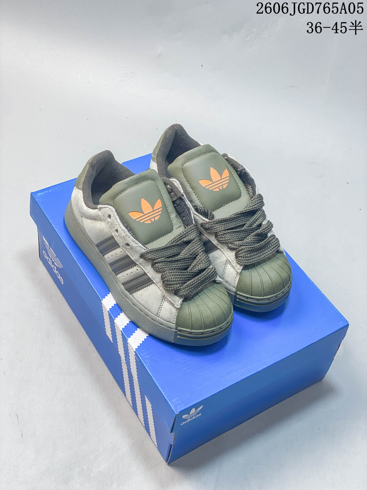 Pair of olive and gray Adidas Originals Superstar XLG sneakers with orange trefoil accents, shown on a blue shoe box