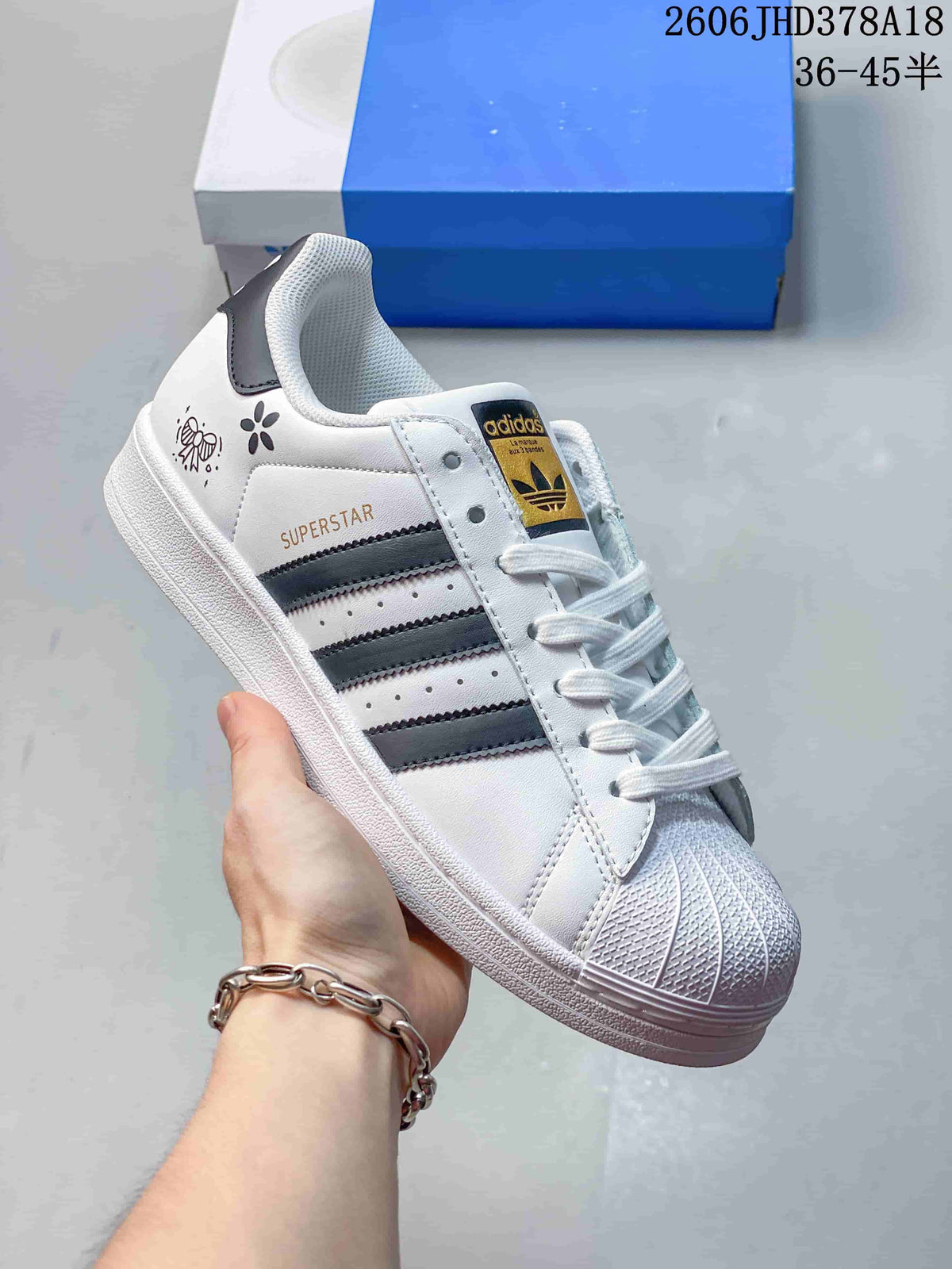 Angled view of the white Superstar sneaker with black stripes and shell toe