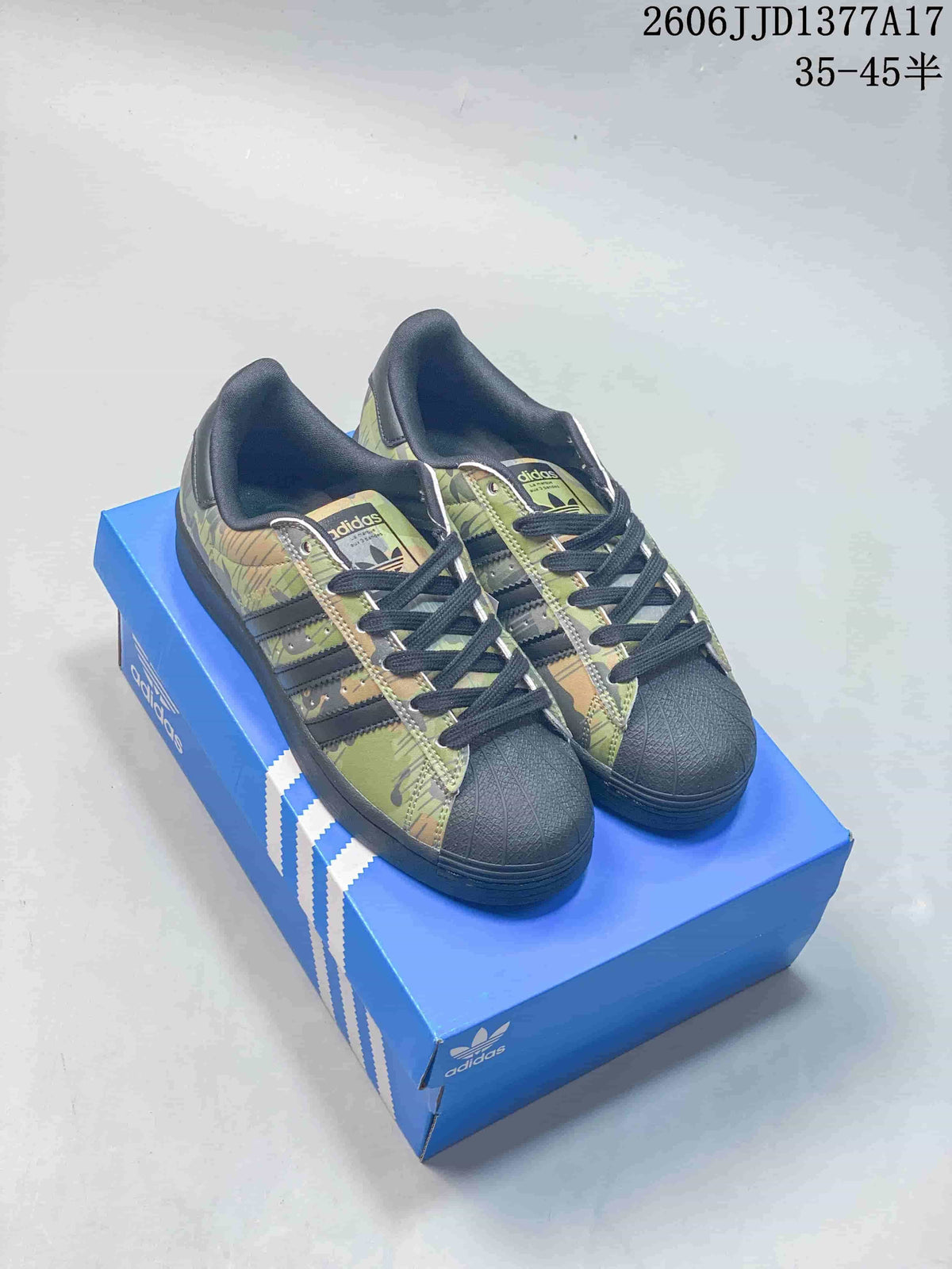 Pair of green camouflage adidas Originals Superstar low-top sneakers with dark shell toes, shown on a blue box