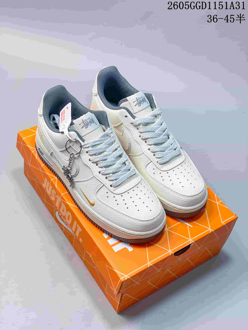 Pair of off-white Nike Air Force 1 low-top style sneakers with grey accents and a metal charm, shown on an orange shoe box