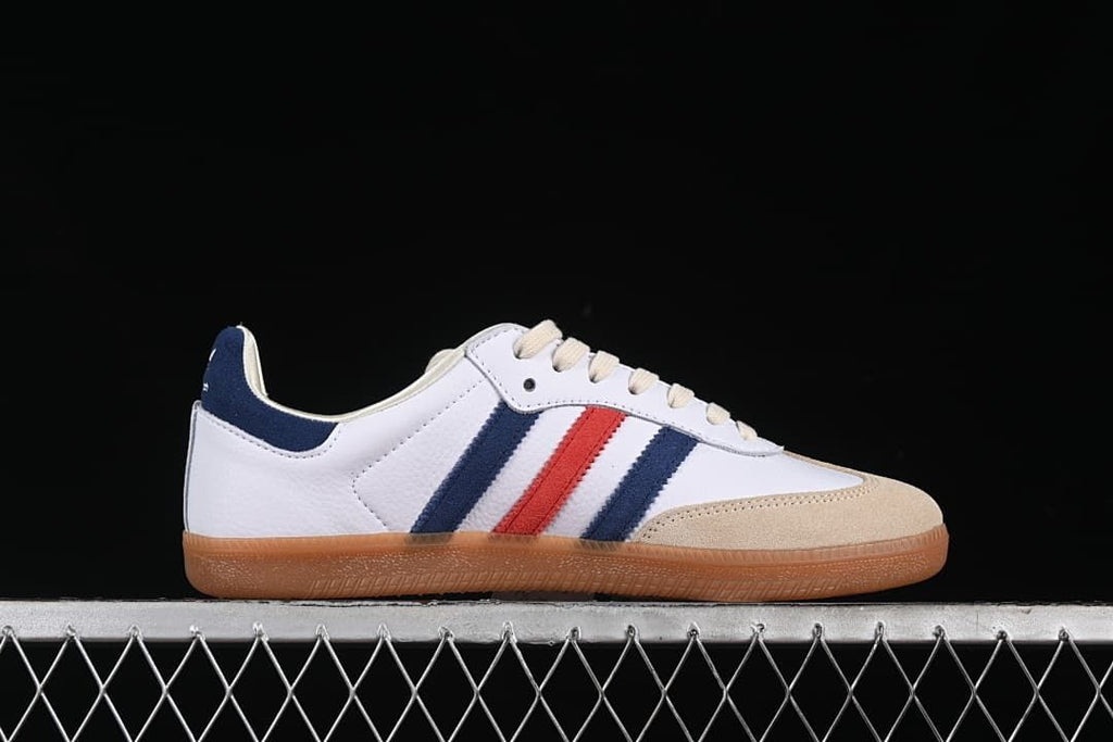 Side profile highlighting the white upper, navy and red stripes, sand-colored toe overlay, and gum sole