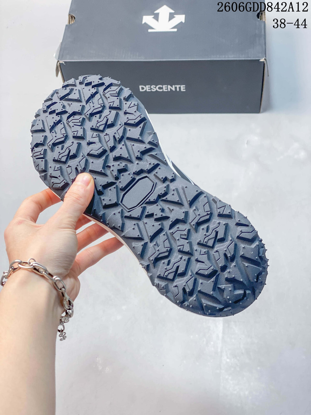 Close-up of the deeply patterned outsole of a gray DESCENTE sneaker, with the branded shoe box behind it.