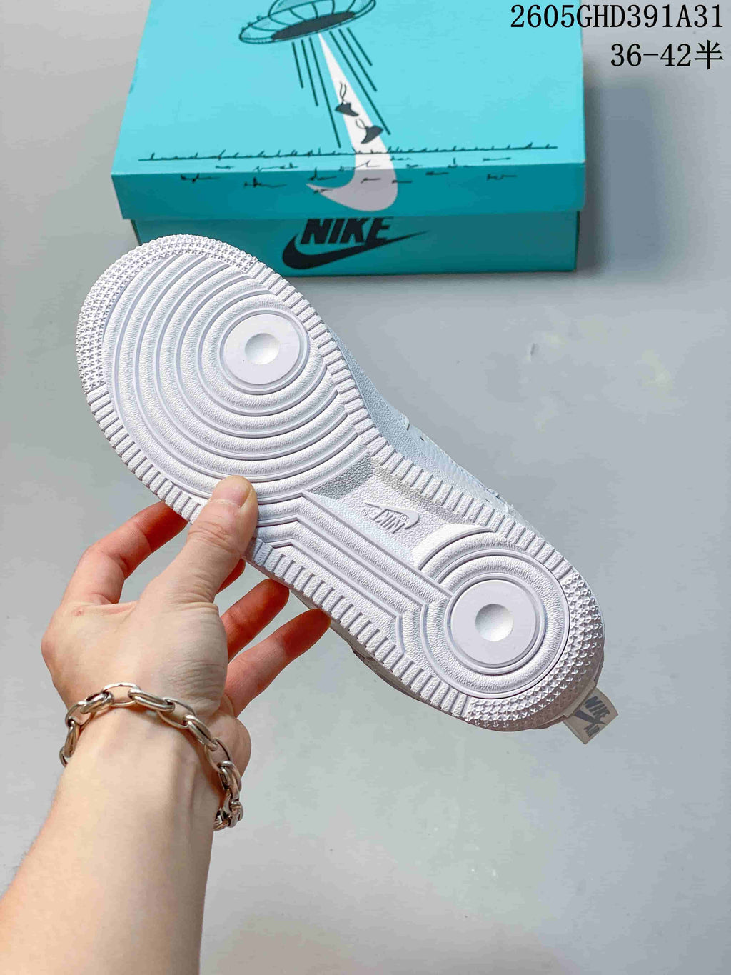 White rubber outsole of a Nike Air Force 1 Low sneaker, with a turquoise illustrated shoebox in the background