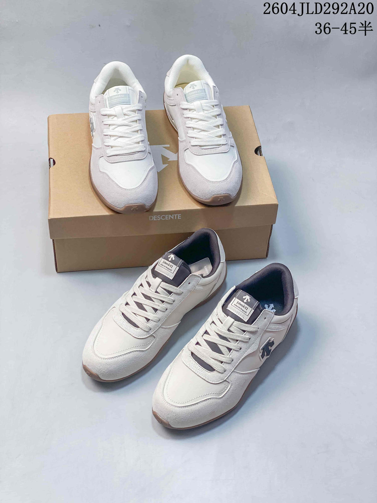 Two pairs of white and pale gray Descente low-profile sneakers displayed with a branded box.