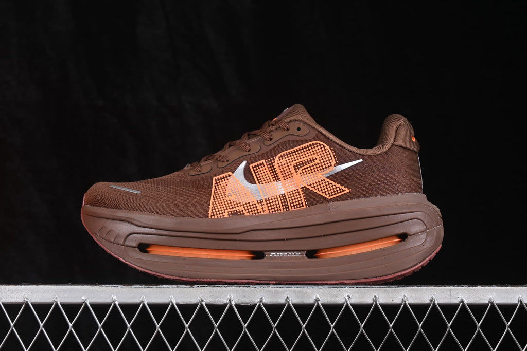 Side profile of the brown and orange Nike sneaker showing its layered thick sole, side graphics, and visible cushioning window.