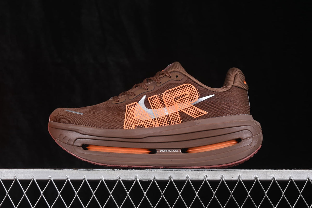 Side profile of the brown and orange Nike sneaker showing its layered thick sole, side graphics, and visible cushioning window.
