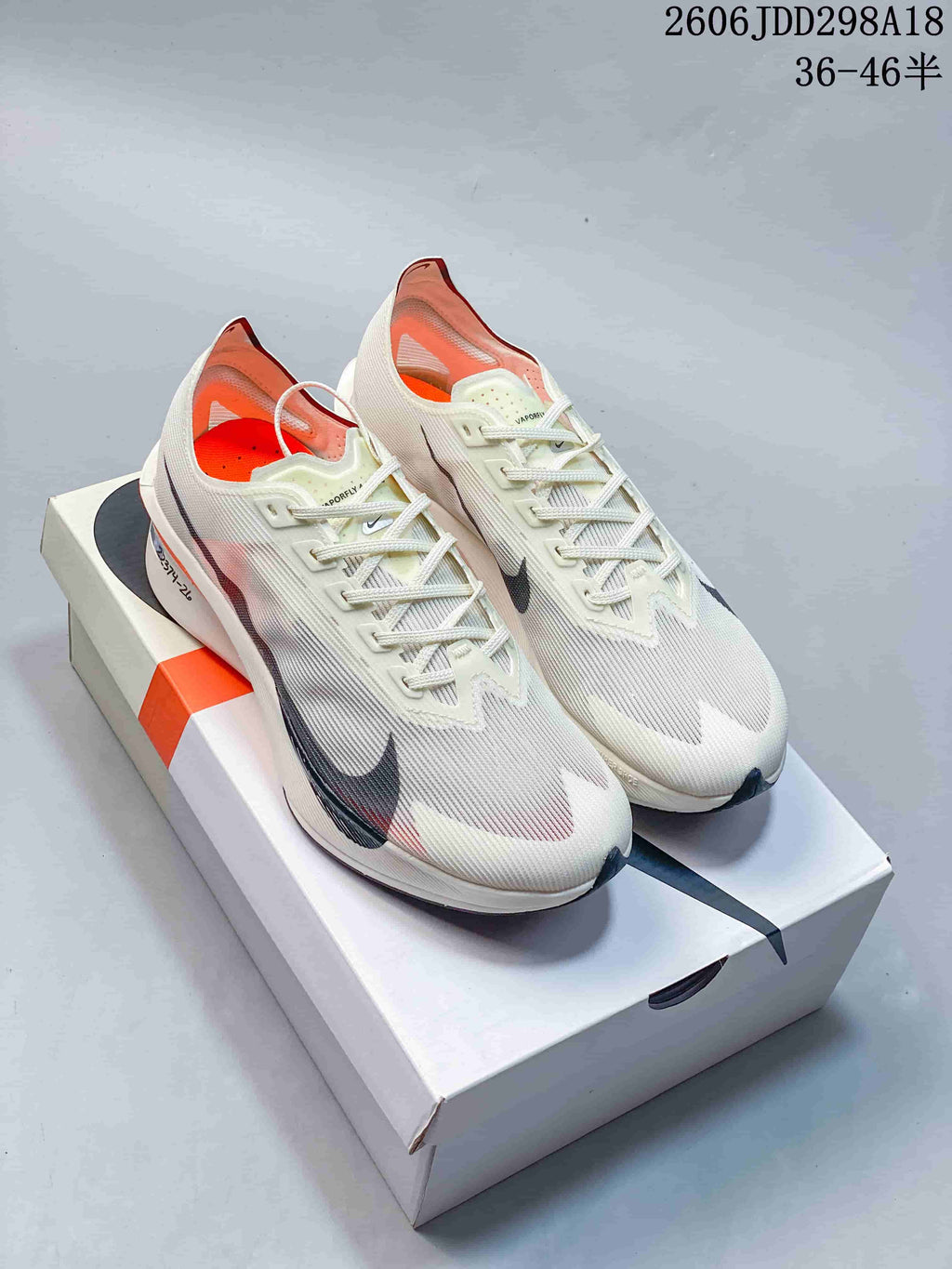 Pair of cream Nike Vaporfly running shoes with dark Swoosh details and orange accents displayed on a box