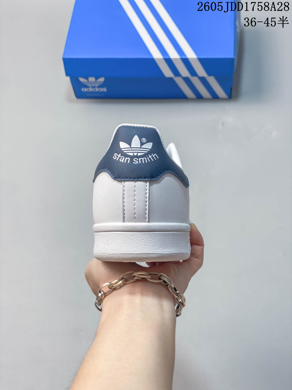 Rear view of a white sneaker with a dark blue heel tab bearing Stan Smith text.