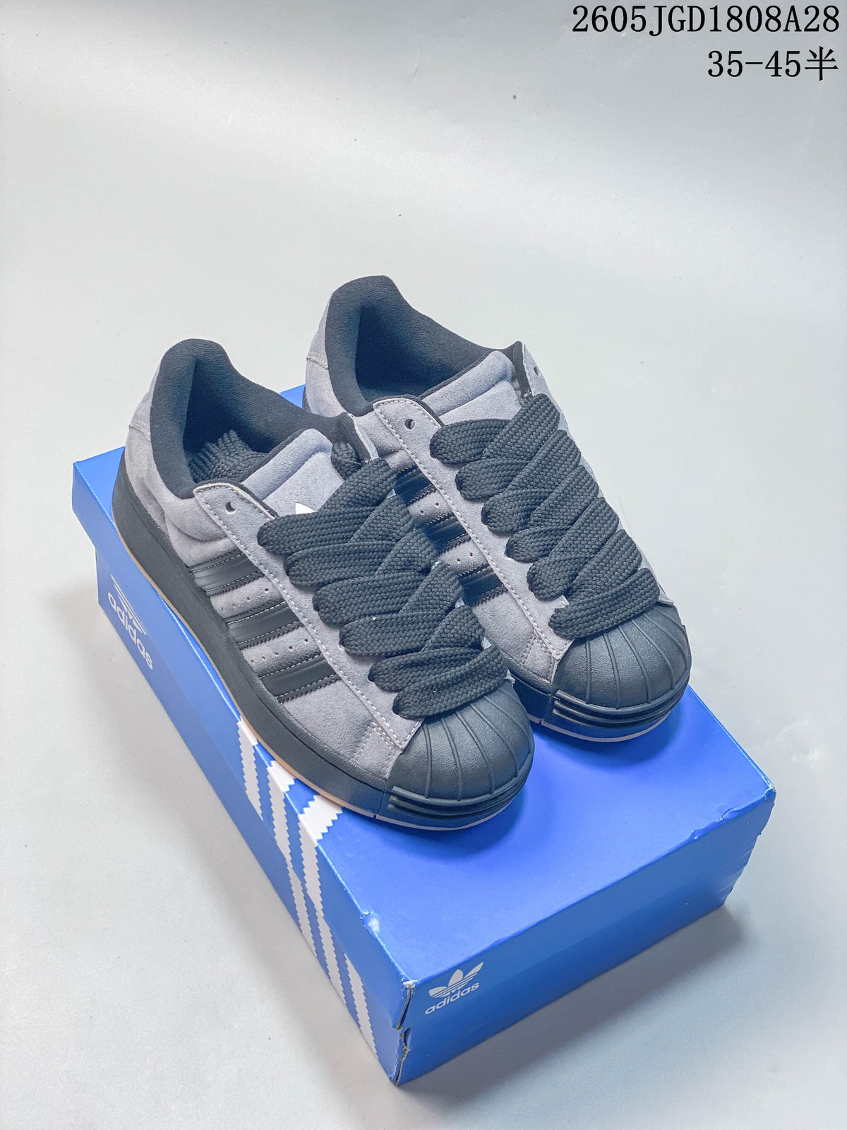Pair of grey Adidas Originals Superstar low-top shoes with dark laces and shell toes, shown on a blue shoe box.