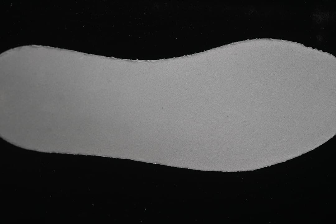 Plain light-colored shoe insert shown against a dark background