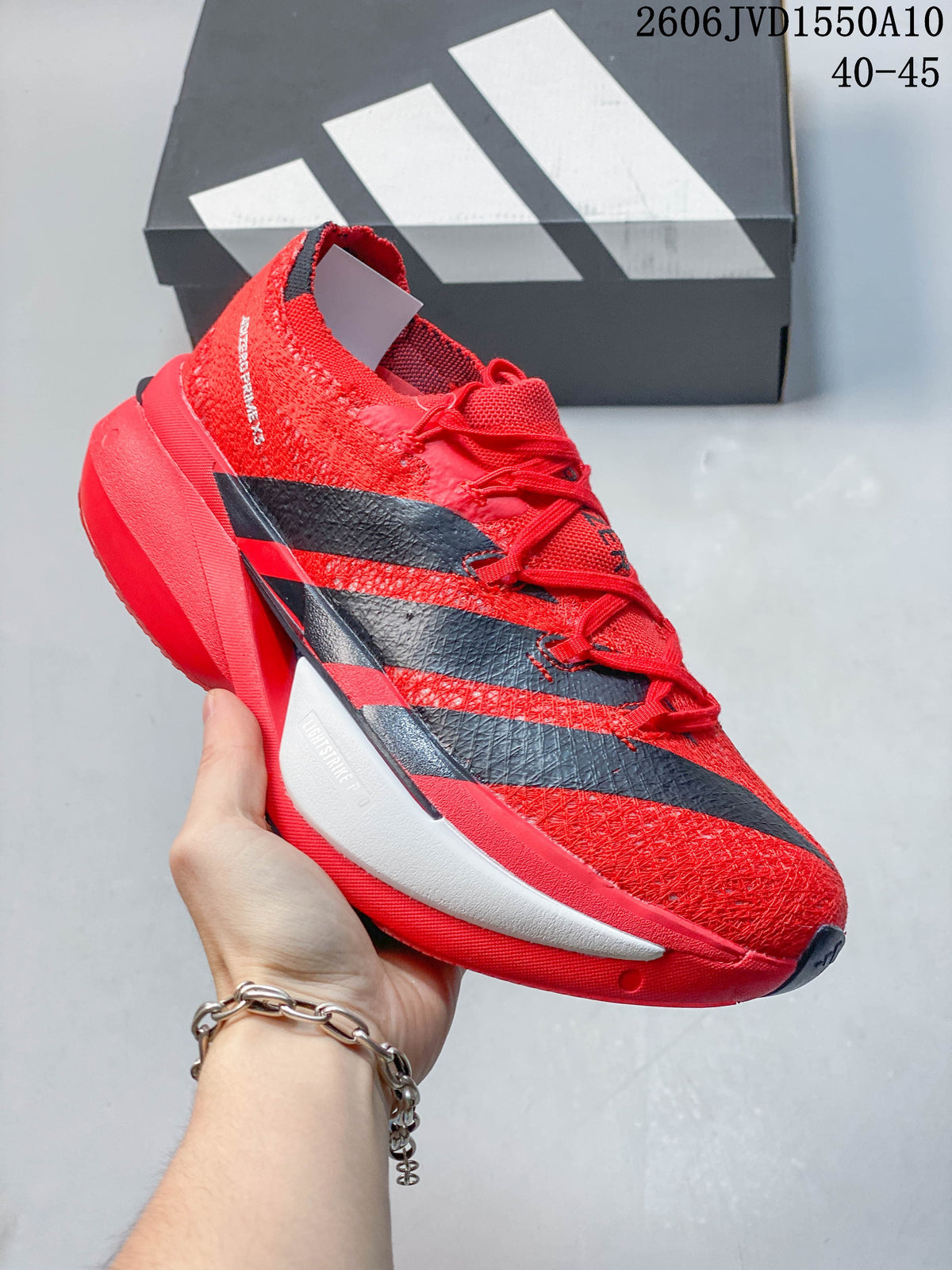 Close side view of a red adidas Adizero Prime X3 running shoe with black stripes and a sculpted midsole.