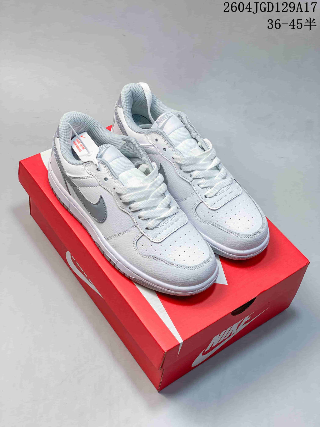 White Nike Big Low sneakers with gray Swooshes displayed on a red shoe box.