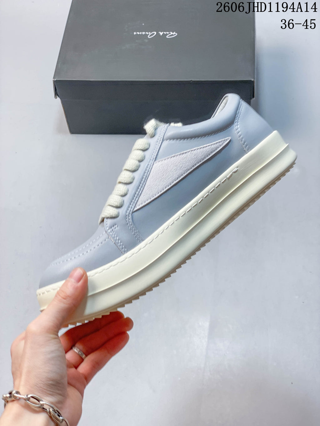 Side view of a pale gray low-top sneaker with a white pointed side panel and off-white sole