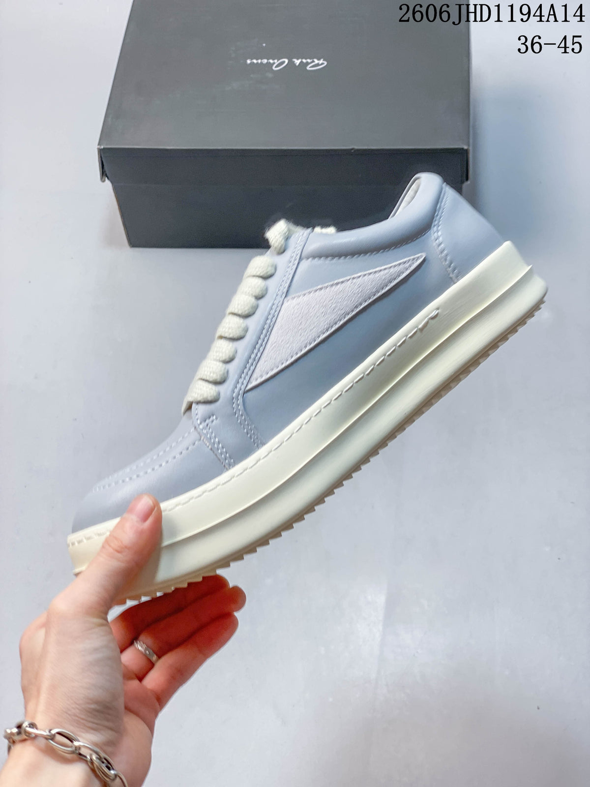 Side view of a pale gray low-top sneaker with a white pointed side panel and off-white sole