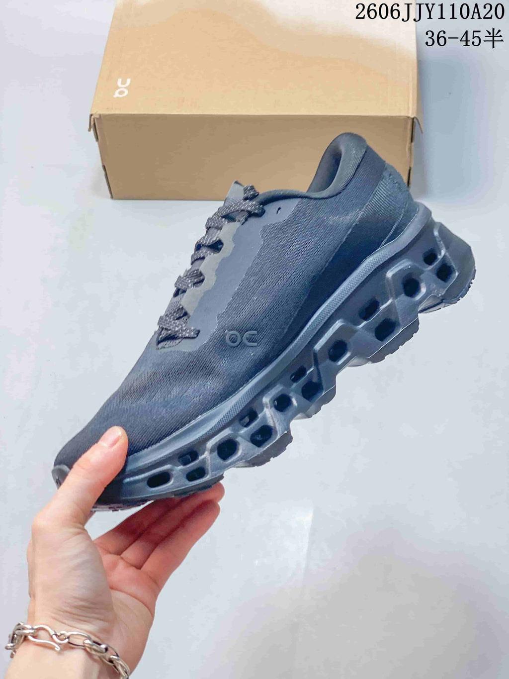 Side view of a dark gray On Cloudmonster 3 shoe with a lace-up front and hollow-section outsole.