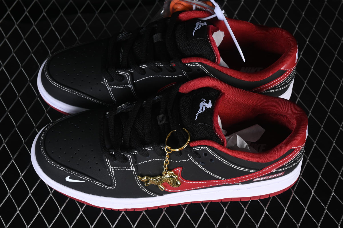 Black and red Nike SB Dunk Low sneakers with white contrast stitching and a gold horse-shaped lace charm