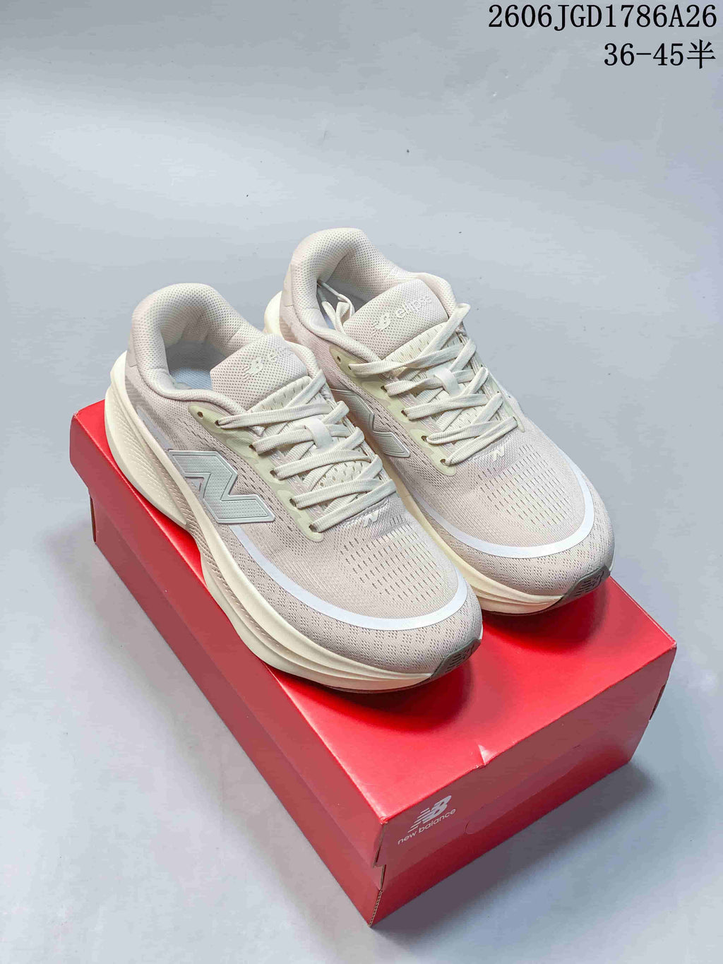 Pair of light neutral New Balance Ellipse V1 low-top running shoes shown on a red shoe box.