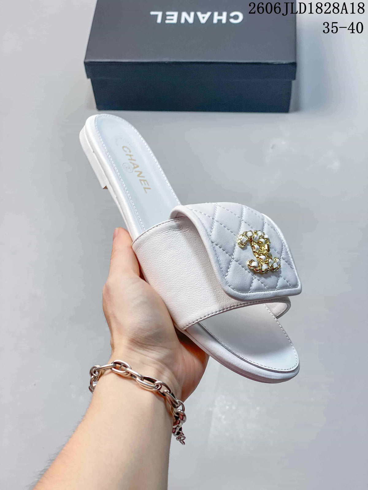 Close-up of a white slide sandal showing its quilted vamp panel, decorative motif, and open toe.