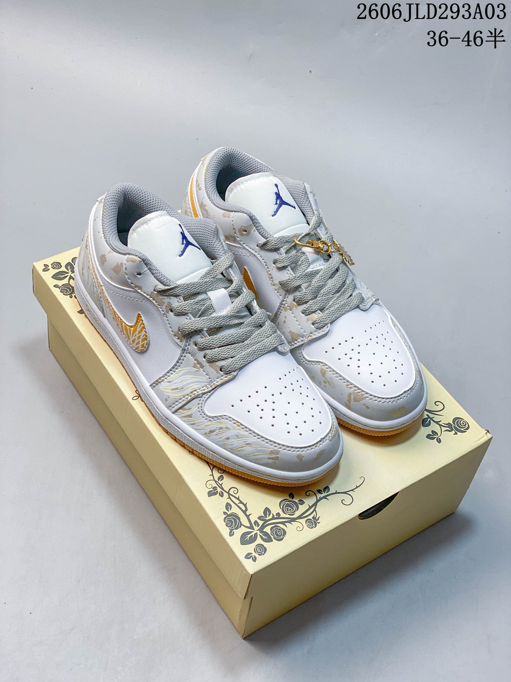 Pair of white and light gray Jordan low-top sneakers with gold-toned details and gum-colored outsoles