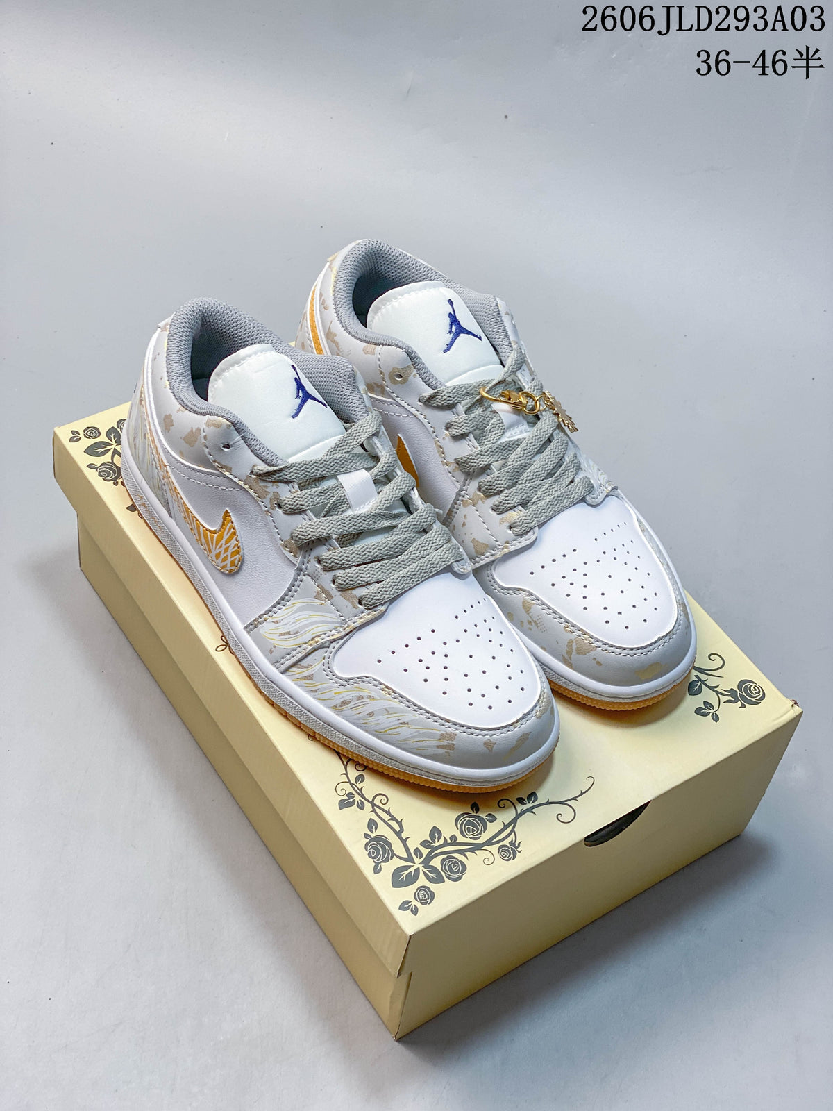 Pair of white and light gray Jordan low-top sneakers with gold-toned details and gum-colored outsoles