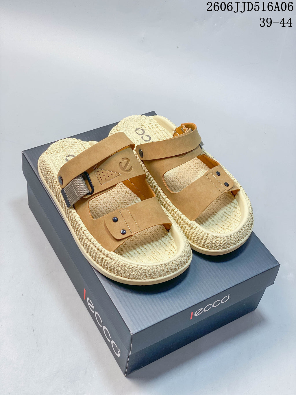 Pair of tan and cream two-strap sandals displayed on a branded shoe box.
