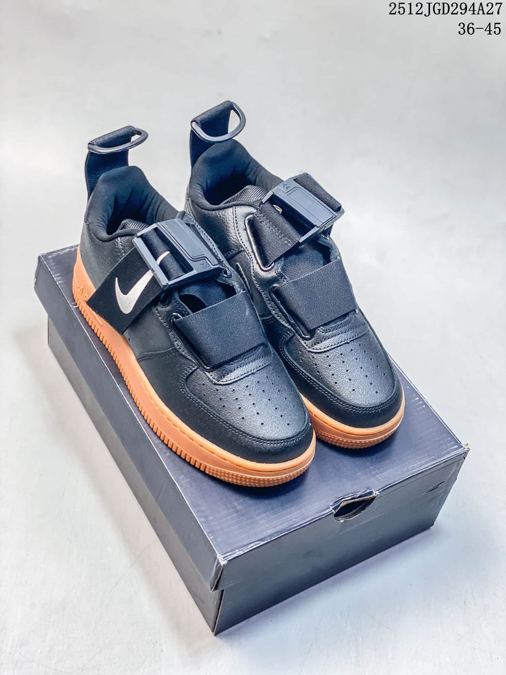Pair of black Nike Air Force 1 Utility sneakers with white Swoosh accents, strap closures, and orange soles