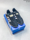 Pair of dark navy Adidas Handball Spezial sneakers with light side stripes and brown outsoles on a blue shoe box.