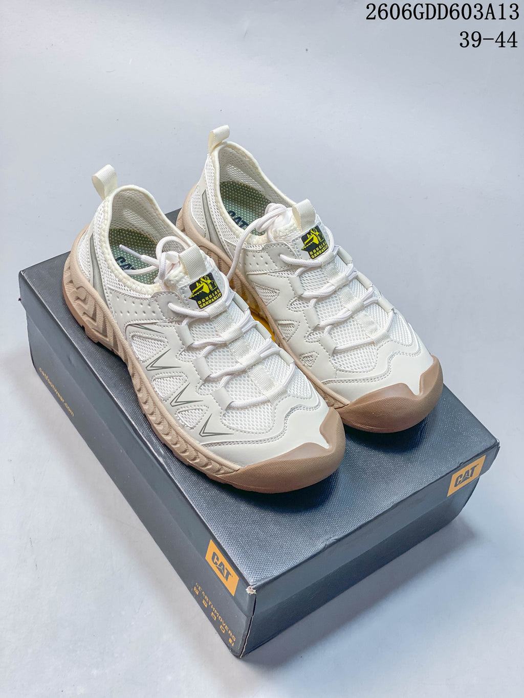 Pair of white and beige CAT lace-up sneakers displayed on a CAT shoe box