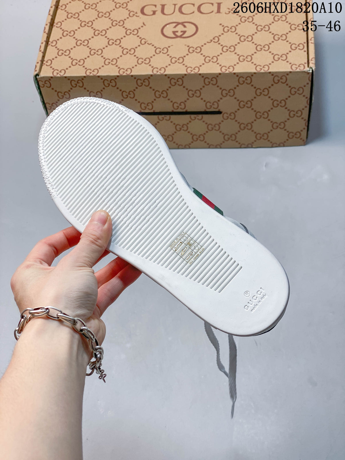 Underside of a white sneaker showing a ridged sole, with a patterned shoe box behind it.