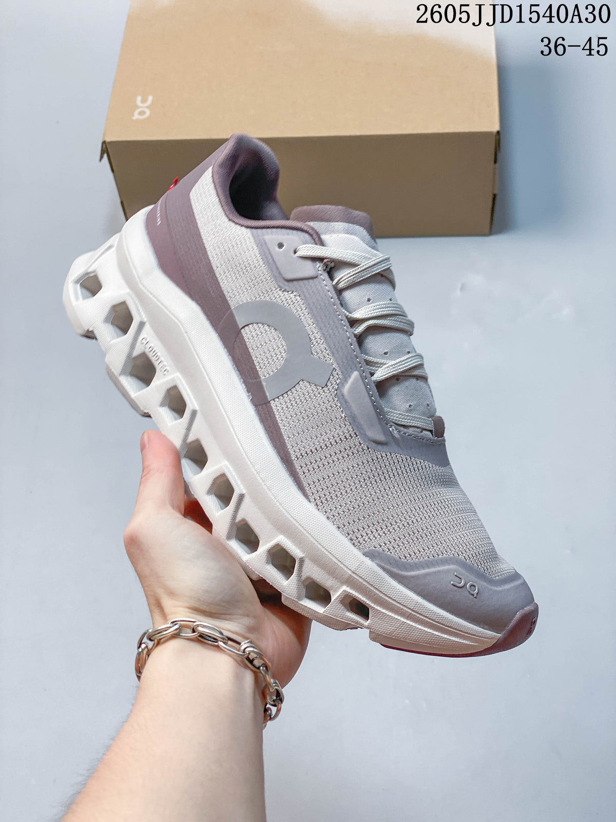 Side view of a pale gray and white On Cloudmonster 2 shoe with muted mauve accents and an open-channel sole.