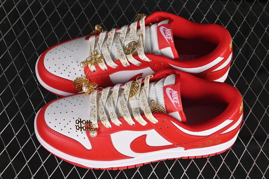 Pair of red and white Nike Dunk Low sneakers with patterned laces and gold-tone accents