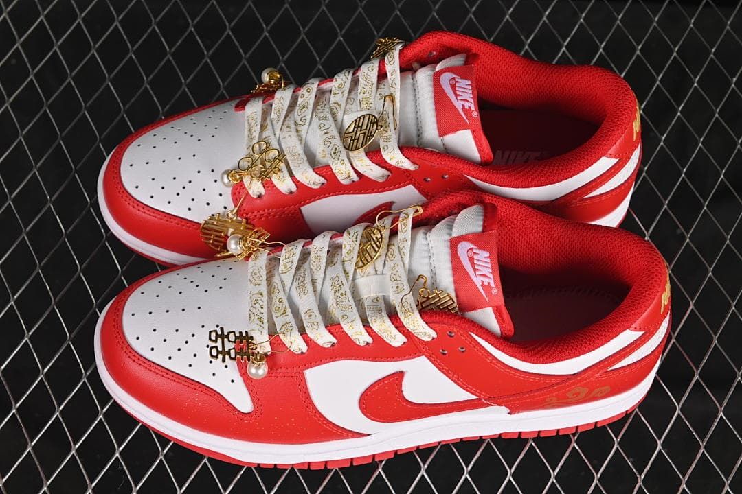 Pair of red and white Nike Dunk Low sneakers with patterned laces and gold-tone accents