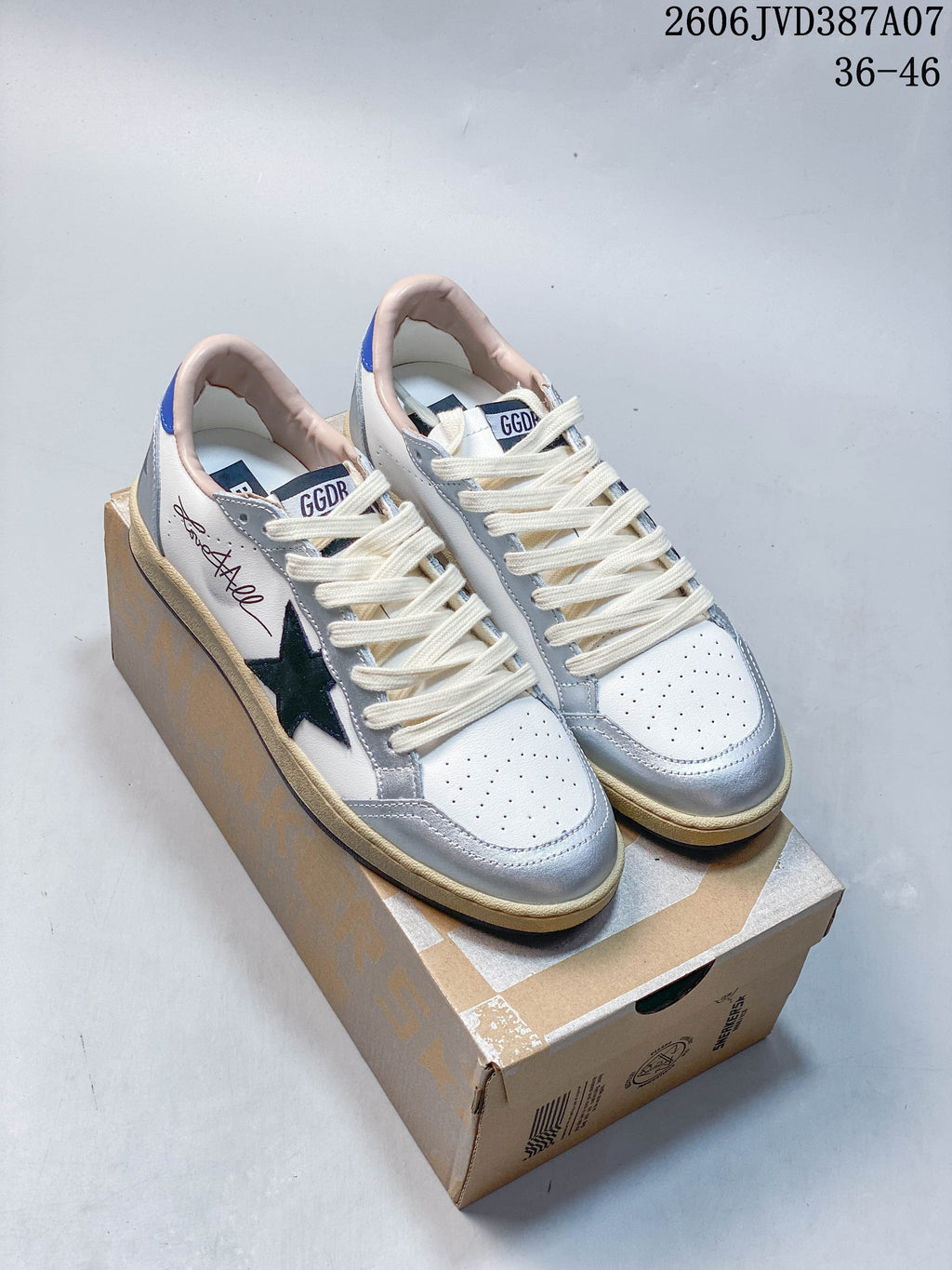 Pair of white and silver Golden Goose Super-Star low-top sneakers with dark star details, blue accents, and cream-colored laces