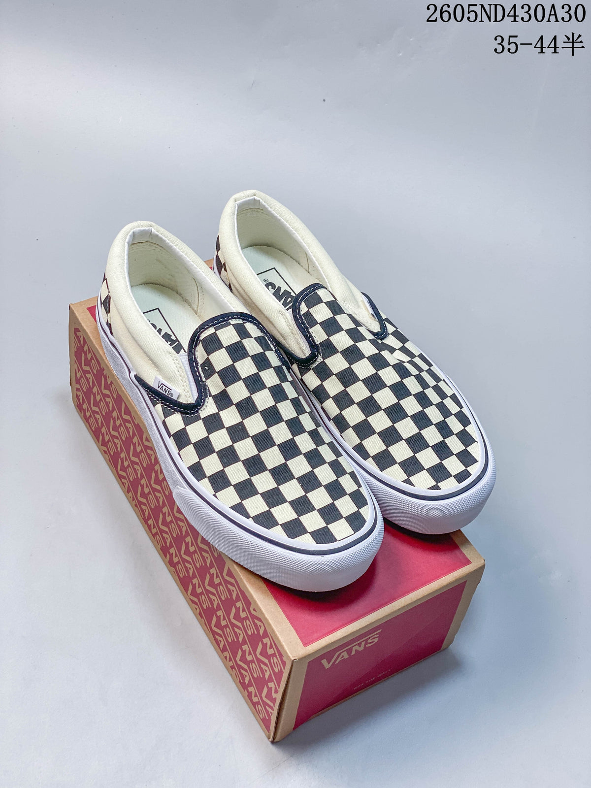 Black-and-white checkerboard Vans slip-on sneakers with raised white soles shown on a branded box.